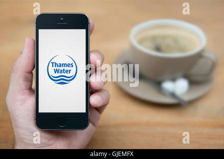 Un uomo guarda al suo iPhone che visualizza la Thames Water logo, mentre sat con una tazza di caffè (solo uso editoriale). Foto Stock