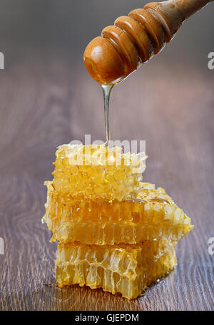 Il miele che gocciola dalla un di legno drizzler oltre il favo di miele Foto Stock