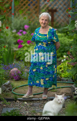 Una donna anziana sta nel suo giardino. Foto Stock