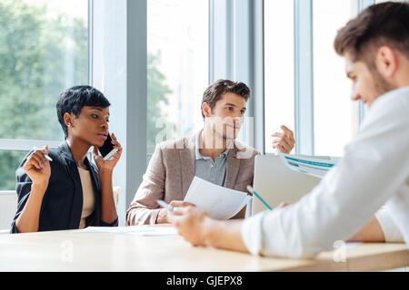 Gruppo multietnico di giovani imprenditori parlando al telefono cellulare e lavorare insieme in ufficio Foto Stock