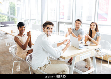 Il gruppo di allegro young business persone sedute e battendo le mani durante la presentazione di office Foto Stock
