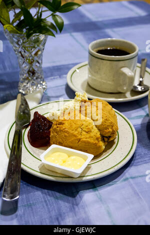 Scones con panna e marmellata sulla tovaglia blu e la tazza di caffè con la brocca del latte Foto Stock