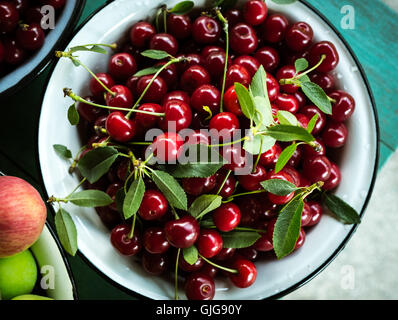 Ciotola riempita con ciliegie organico sul tavolo verde sullo sfondo Foto Stock
