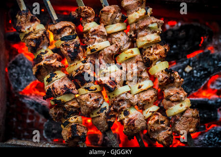 Barbecue spiedini di carne di maiale sul grill caldo close-up. Fiamme di fuoco e i carboni in background Foto Stock