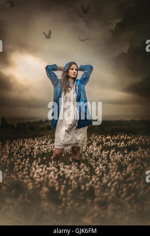 Giovane donna in blu Giacca pioggia in piedi nei campi Foto Stock