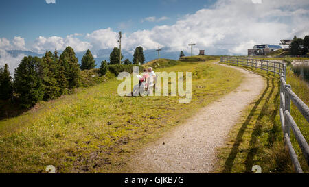 Una coppia senior in appoggio su una panca in legno cercando di una mappa su un paesaggio di montagna Foto Stock