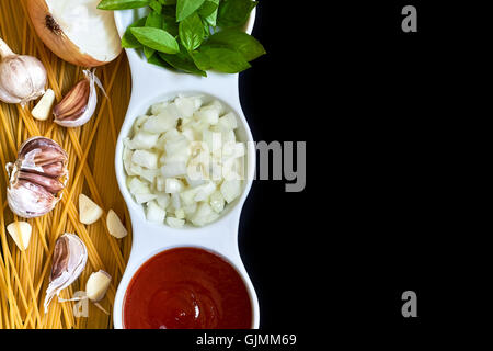 Il basilico e la cipolla tagliata a fette e passata di pomodoro in bianco ciotola con materie Spaghetti aglio e sparse su sfondo nero. Concetto Foto Stock