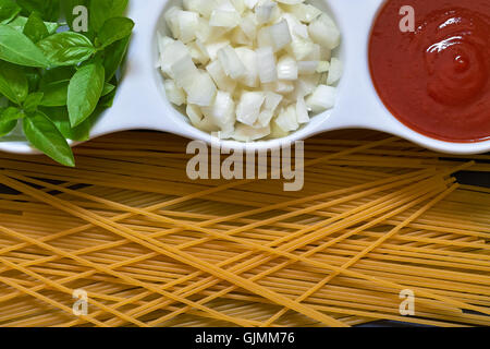 Il basilico e la cipolla tagliata a fette e passata di pomodoro in bianco ciotola con materie spaghetti sparsi intorno. Concetto di immagine per la cucina italiana. Parte superiore Foto Stock