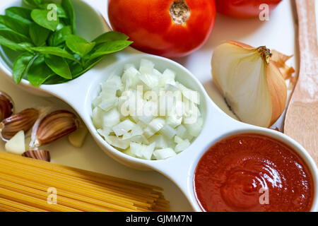 Il basilico e la cipolla tagliata a fette e passata di pomodoro in bianco ciotola con materie Spaghetti aglio e sparse su sfondo bianco. Concetto Foto Stock