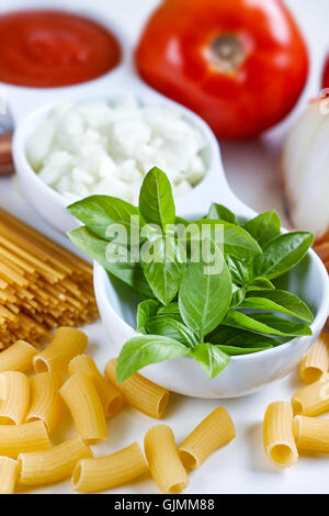 Il basilico e la cipolla tagliata a fette e passata di pomodoro in bianco ciotola con pasta cruda e aglio disseminate su sfondo bianco Foto Stock