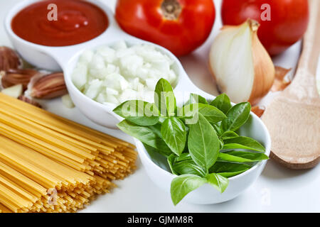 Il basilico e la cipolla tagliata a fette e passata di pomodoro in bianco ciotola con materie Spaghetti aglio e sparse su sfondo bianco Foto Stock