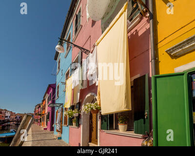 Case con terrazza in riva al mare dipinte con colori vivaci e lavanderia appesa all'esterno sulle linee di lavaggio dell'isola di Burano. Venezia, Italia. Foto Stock