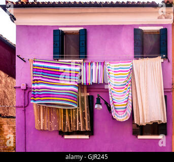 Casa dipinta di viola con colorata biancheria a righe appesa all'esterno sulle linee di lavaggio. Isola di Burano. Venezia, Italia Foto Stock