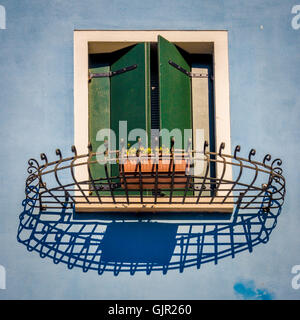 Verde scuro parzialmente aperto persiane finestre su una parete esterna blu pallido reso di casa tradizionale sull'isola di Burano. Italia. Foto Stock