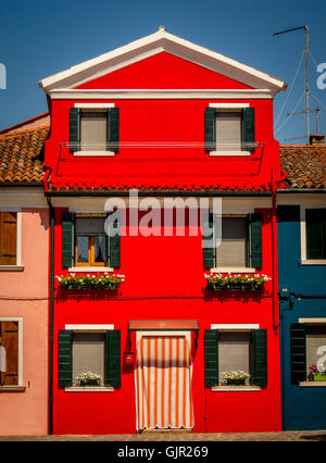 Persiane di verde scuro su una parete esterna di rosso chiaro reso della casa tradizionale sull'isola di Burano. Italia. Foto Stock