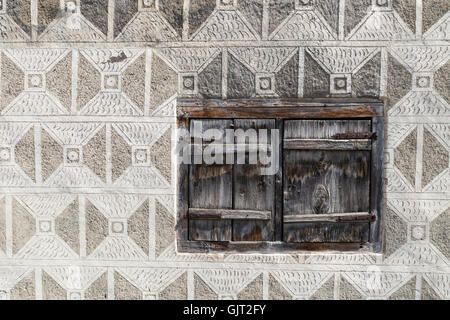 Un muro di una casa rurale con i tradizionali ornamenti intricati e una piccola finestra con persiane in legno. La parte orientale della Svizzera. Foto Stock
