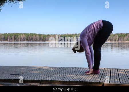 Pretty Woman rendendo semplice lo Yoga asana sul molo di legno della foresta sulla riva del lago Foto Stock
