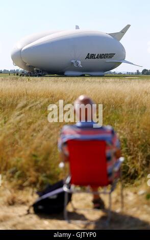 Un uomo prende il suo posto come preparazioni sono fatte per il volo inaugurale del Airlander 10, aeromobili più grandi al mondo, a Cardington airfield nel Bedfordshire. Foto Stock