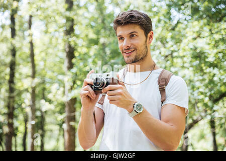 Felice giovane con uno zaino di scattare le foto con la vecchia foto fotocamera nella foresta Foto Stock