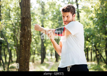 Atletica Giovane sportivo con telefono cellulare in handband permanente e fare gli esercizi in foresta Foto Stock