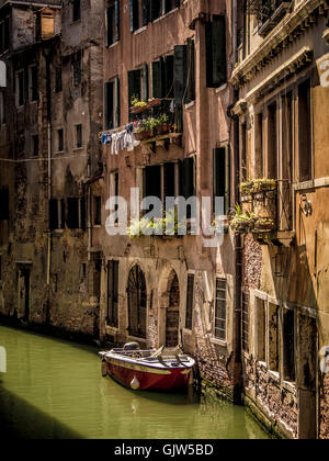 Unico ormeggiate barche a motore sul stretto canale con vecchi edifici tradizionali, con biancheria appesa al di fuori. Venezia, Italia. Foto Stock
