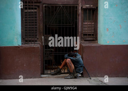 Un povero uomo dorme in una posizione da seduto su una strada nella Vecchia Havana, Cuba Foto Stock