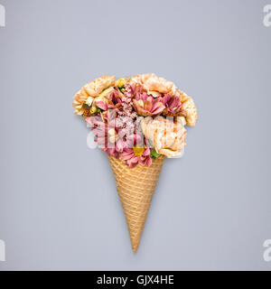 Creative ancora in vita di un gelato cono di cialda con fiori su sfondo grigio. Foto Stock