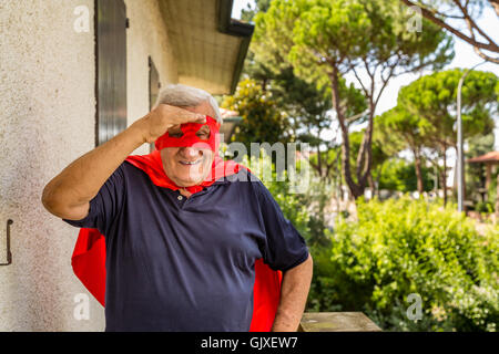 Un vecchio uomo vestito come un supereroe la scansione l'orizzonte dal balcone della sua casa Foto Stock