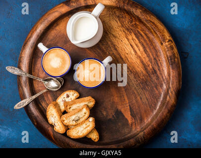 Caffè espresso Caffè in tazze con biscotti e latte nel bricco in legno che serve round scheda sopra blu scuro Compensato verniciato background, Foto Stock