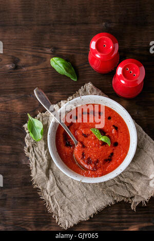 Piastra bianca di freddo fresco di pomodoro Zuppa Gazpacho con basilico e balsamico, servita con rosso sale e pepe su un letto di sacco uovere Foto Stock