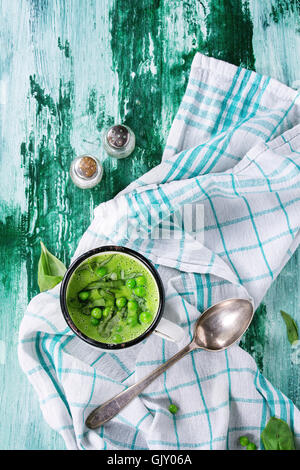 Vintage bianco mug con crema di piselli zuppa con fette di basilico, servito con il cucchiaio, il sale e il pepe bianco asciugamano da cucina sopra Foto Stock