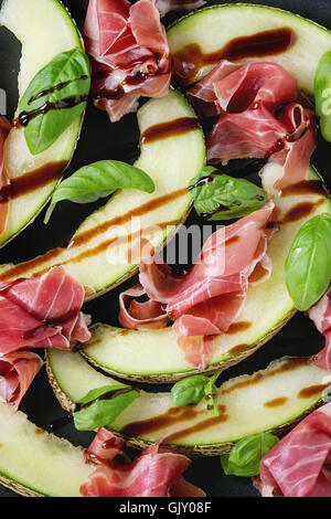 Sfondo di cibo con fette di melone e Prosciutto, foglie di basilico e sauceClose balsamico fino. Vista dall'alto. Foto Stock