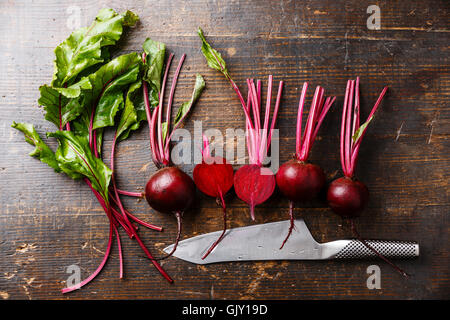 La barbabietola rossa con herbage foglie verdi e coltello da cucina su sfondo di legno Foto Stock