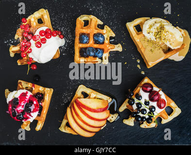 Belga caldo waffles fatti in casa con giardino fresco di bacche e frutta e gelato su ardesia scura sullo sfondo di pietra, vista dall'alto Foto Stock