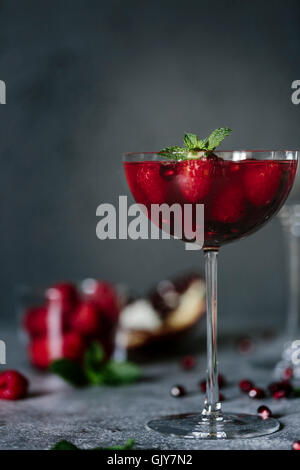 Un vetro del coupé di lampone e Melograno Champagne Cocktailed guarnita con la menta è fotografata dalla vista frontale. Foto Stock