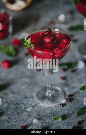 Un vetro del coupé di lampone e Melograno Champagne Cocktailed guarnita con la menta è fotografata dalla vista frontale. Foto Stock