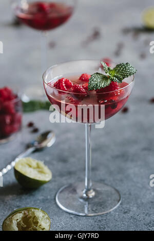 Un vetro del coupé di lampone e Melograno Champagne Cocktailed guarnita con la menta è fotografato (con altri 2 al di fuori della messa a fuoco) Foto Stock