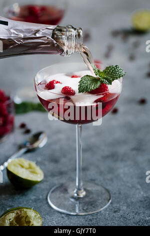 Un bicchiere di lampone e Melograno Cocktail Champagne viene rabboccato con champagne Foto Stock