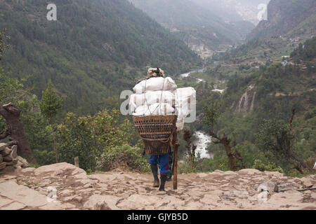 Porter trasporta un carico molto pesante lungo un percorso in Himalaya montagne, Nepal Foto Stock