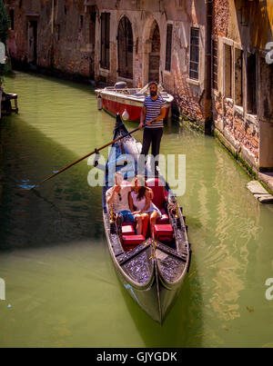 Gondoliere indossando il tradizionale a strisce dello sterzo superiore la sua gondola lungo uno stretto canale di Venezia, Italia. Foto Stock