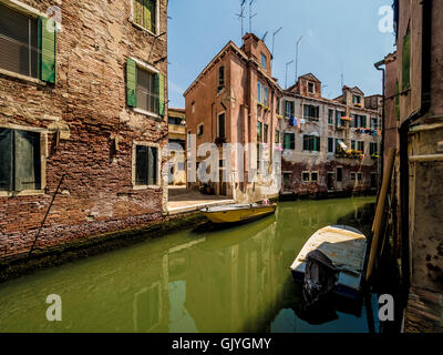 Barche ormeggiate su uno stretto canale con edifici tradizionali su entrambi i lati. Venezia, Italia. Foto Stock