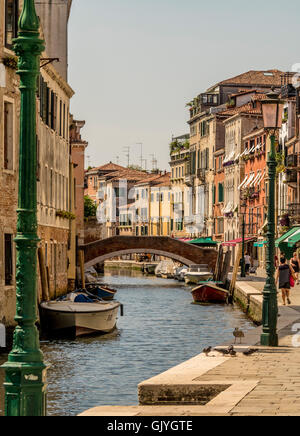 Stretto canale e piede arcuato ponte con edifici tradizionali e barche ormeggiate in corrispondenza di entrambi i lati. Venezia, Italia. Foto Stock