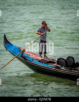 Gondoliere indossando il tradizionale a strisce dello sterzo superiore la sua gondola mentre parli sul suo telefono cellulare. Venezia, Italia. Foto Stock