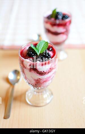 Le coppe di vetro con il formaggio cremoso dessert blackberry. More fresche e foglie di menta sono posti sulla sommità del dessert. Foto Stock