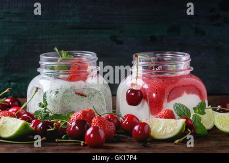 Piazza due vasi di vetro con yogurt fatto in casa con la menta, purea di fragole, ciliegio e semi di chia servita con frutti di bosco freschi e SLI Foto Stock