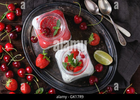 Piazza due vasi di vetro con yogurt fatto in casa con la menta, purea di fragole, ciliegio e semi di chia servita sul vassoio vintage con freschi Foto Stock