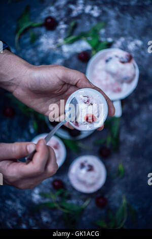 Mani tenendo un cucchiaio e una piccola ciotola di ciliegio fresco gelato. Foto Stock