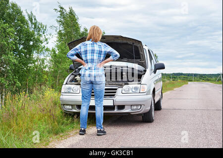 Donna che guarda sotto il cofano della sua auto rotto Foto Stock