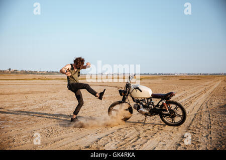 Uomo che fa la polvere in piedi vicino alla sua motocicletta in corrispondenza del deserto Foto Stock