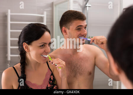 Close-up felice giovane coppia lavarsi i denti in piedi di fronte a specchio nel moderno bagno piastrellato a casa Foto Stock